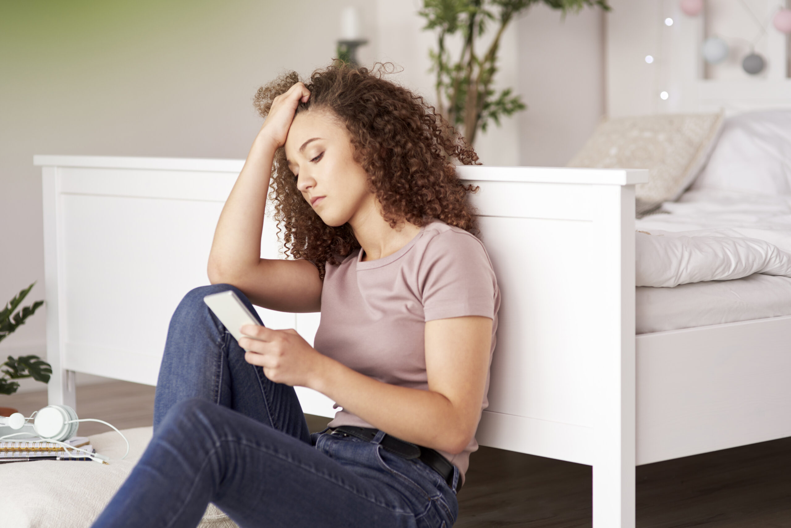 Upset teenage girl sitting on her bedroom floor on her phone